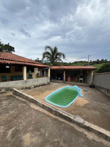 Área externa com piscina verde, casa térrea com varanda e céu nublado.
