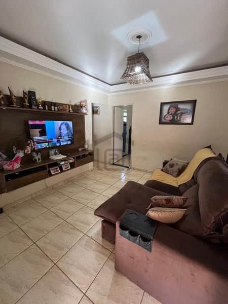 Sala aconchegante com sofá marrom, TV e piso cerâmico claro. Decoração clean e iluminação suave.