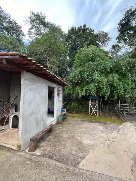 Área externa com construção rústica em concreto, bancos de madeira e vegetação ao fundo.