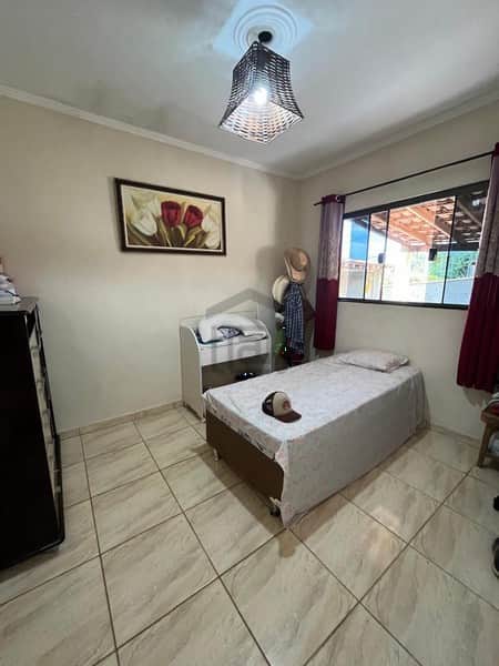 Quarto com cama de solteiro, piso cerâmico e decoração simples. Janela com cortina e pintura na parede.