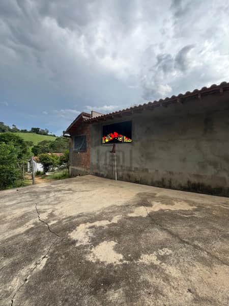 Área externa com piso de concreto rachado. Casa inacabada ao fundo, céu nublado.