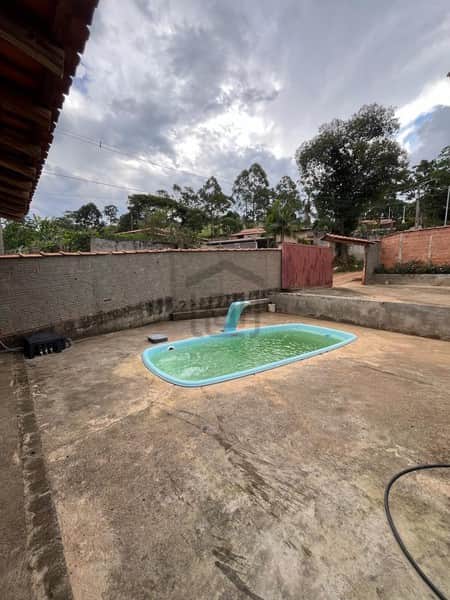 Área externa com piscina azul e cascata, piso de concreto e muro ao fundo. Céu nublado.