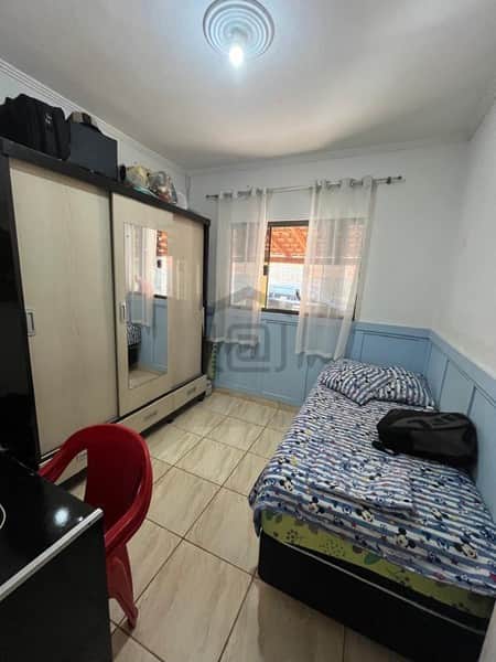 Quarto pequeno com cama de solteiro, guarda-roupa e piso cerâmico claro. Ambiente simples e iluminado.