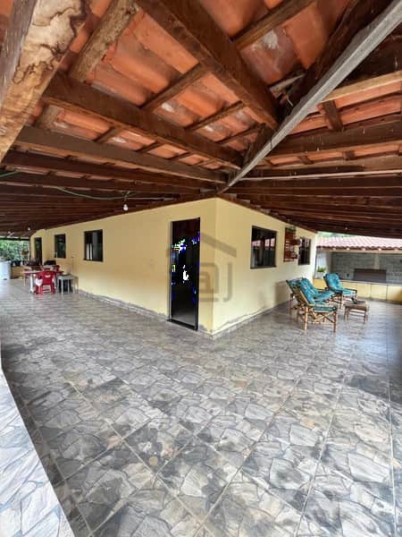Varanda ampla com piso cerâmico, teto rústico e paredes amarelas. Área de lazer com cadeiras e mesas.